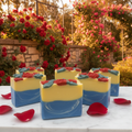 The Enchanted Rose handmade cold process soap bars with yellow and blue layers and red rose embeds in a romantic garden setting with cascading crimson roses and golden hour light