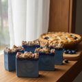 Grandma's Blueberry Pie handmade cold process soap bars with deep blue swirls and crumble topping, cozy kitchen windowsill blueberry pie background